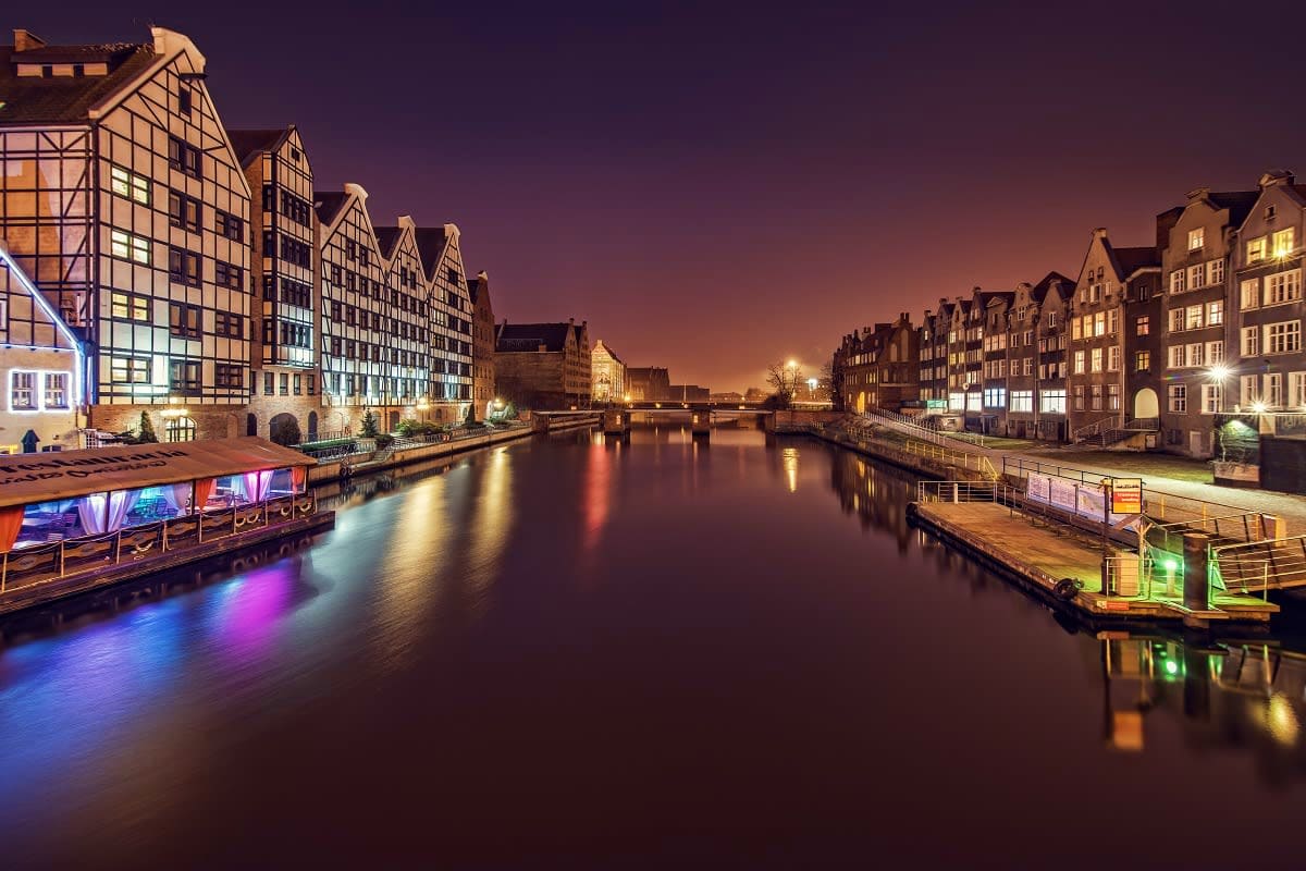 Historic merchant buildings along illuminated Motlawa River waterfront at twilight in Gdansk, Poland