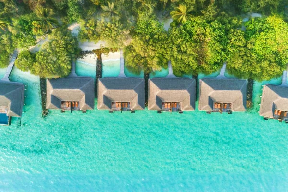 Aerial view of beachfront bungalows with turquoise water and tropical palm trees at a luxury island resort