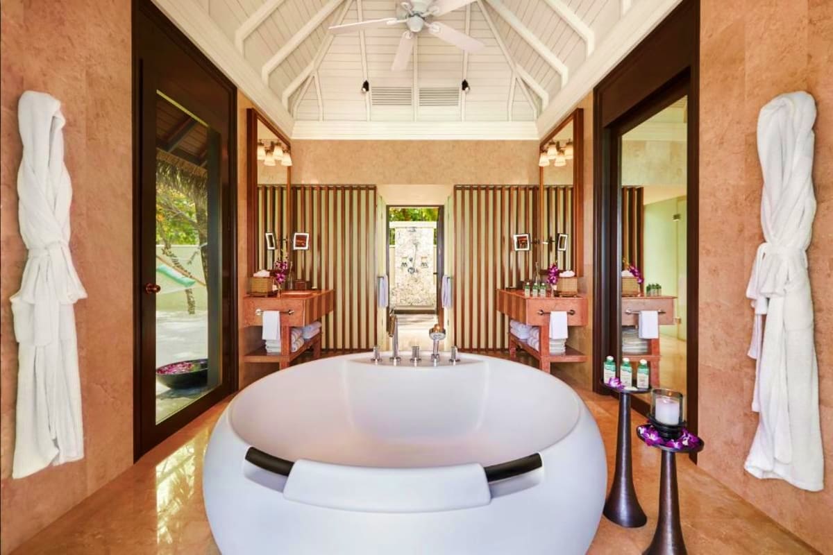 Luxury spa bathroom with round white soaking tub, dual wooden vanities, white towel racks, and vaulted ceiling with skylight