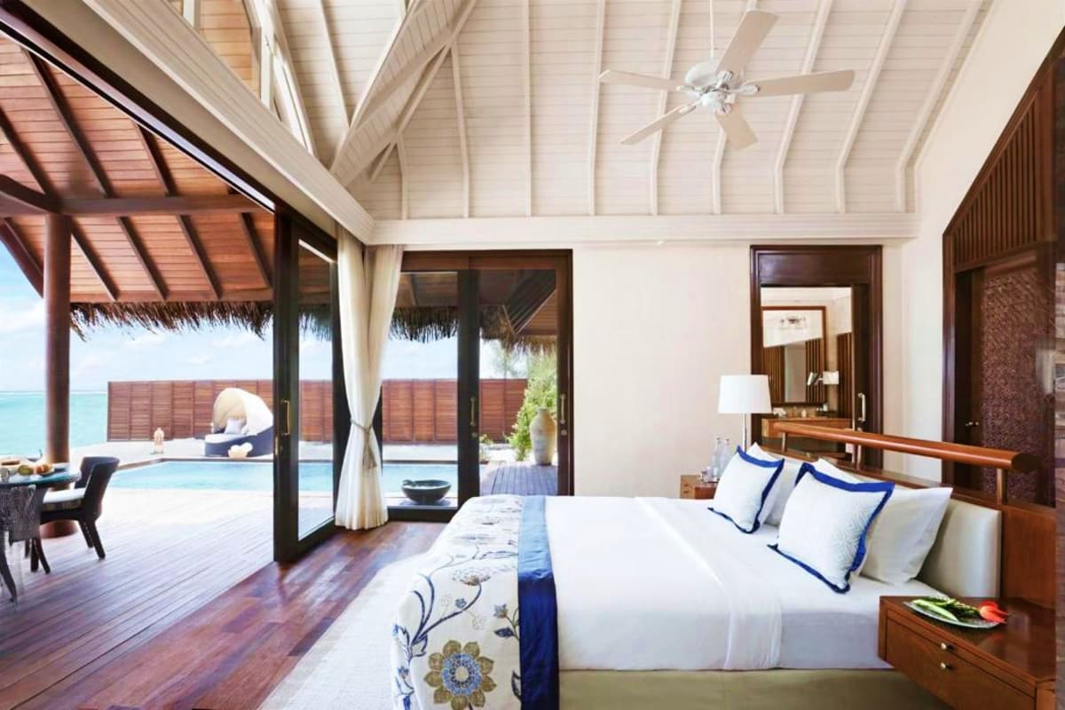 Luxury overwater bungalow bedroom with king bed, ocean view, private pool deck, and thatched roof at tropical resort