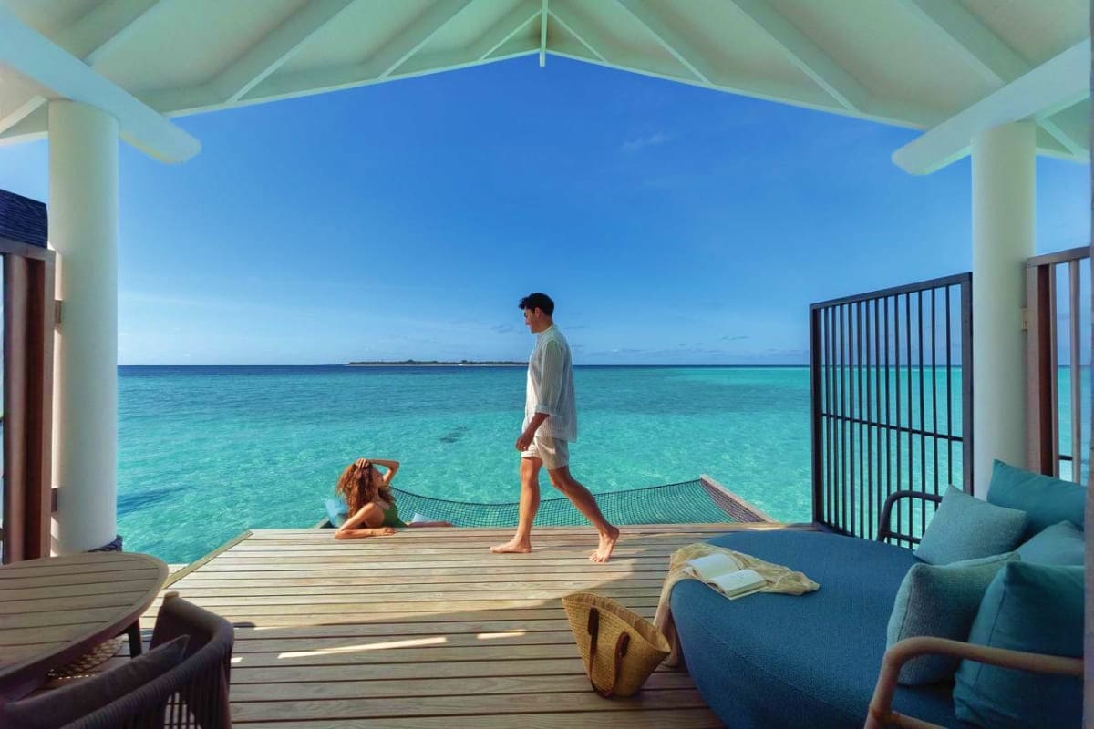 Couple relaxing on wooden deck of overwater bungalow with turquoise lagoon and tropical island view