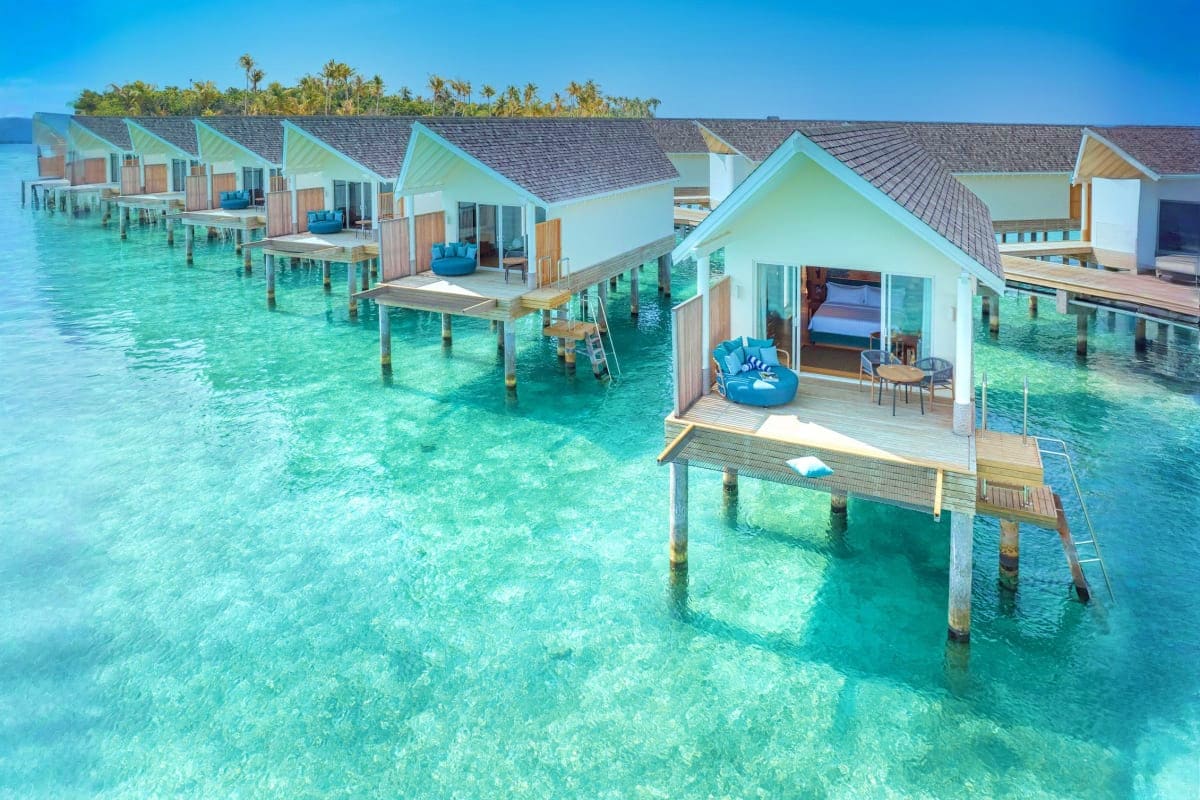 Row of overwater bungalows with turquoise lagoon, wooden decks, and palm trees at tropical resort