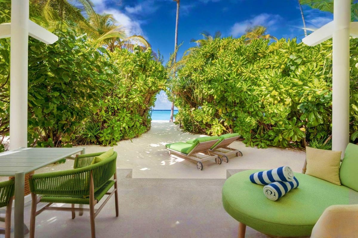 Tropical beach villa patio with green lounge chairs, mangrove vegetation tunnel leading to turquoise ocean water and palm tre