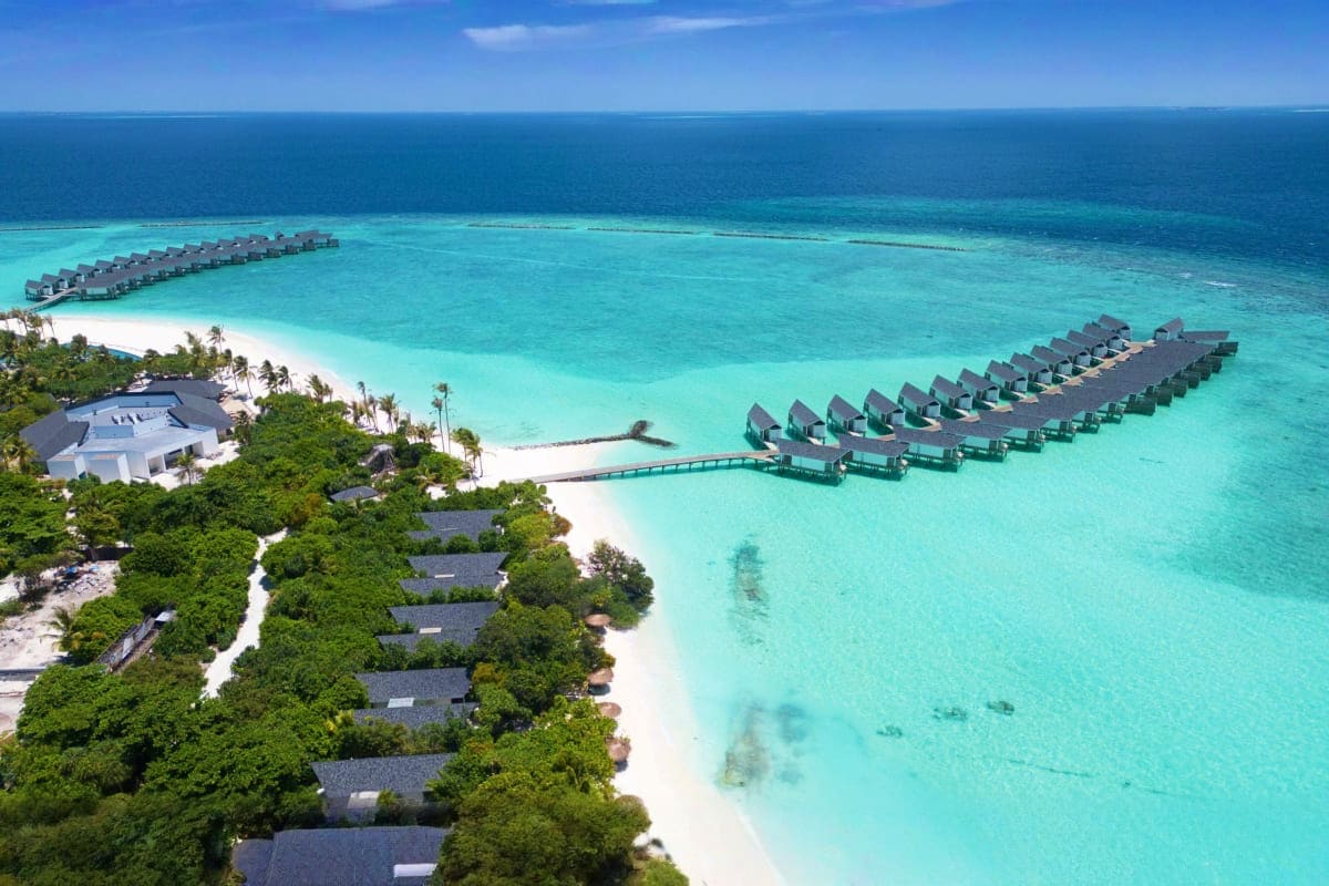 Aerial view of RAAYA resort with overwater bungalows, white sand beach, and turquoise lagoon in the Maldives