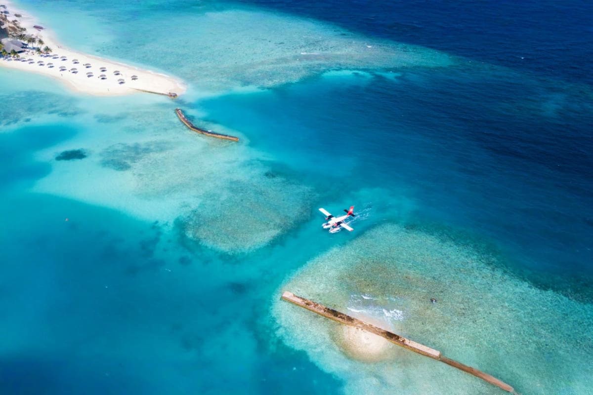Aerial view of tropical island with white sand beach, turquoise water, seaplane, and shipwrecks scattered in the shallow lago