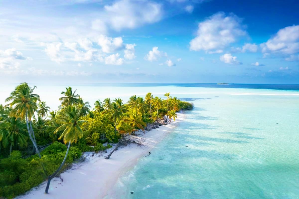 Aerial view of Medhufushi Island Resort showing white sand beach, turquoise lagoon, and palm trees under blue sky