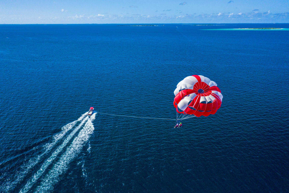 Speedboat towing parasail with red and white parachute over blue ocean waters near tropical island in the Maldives