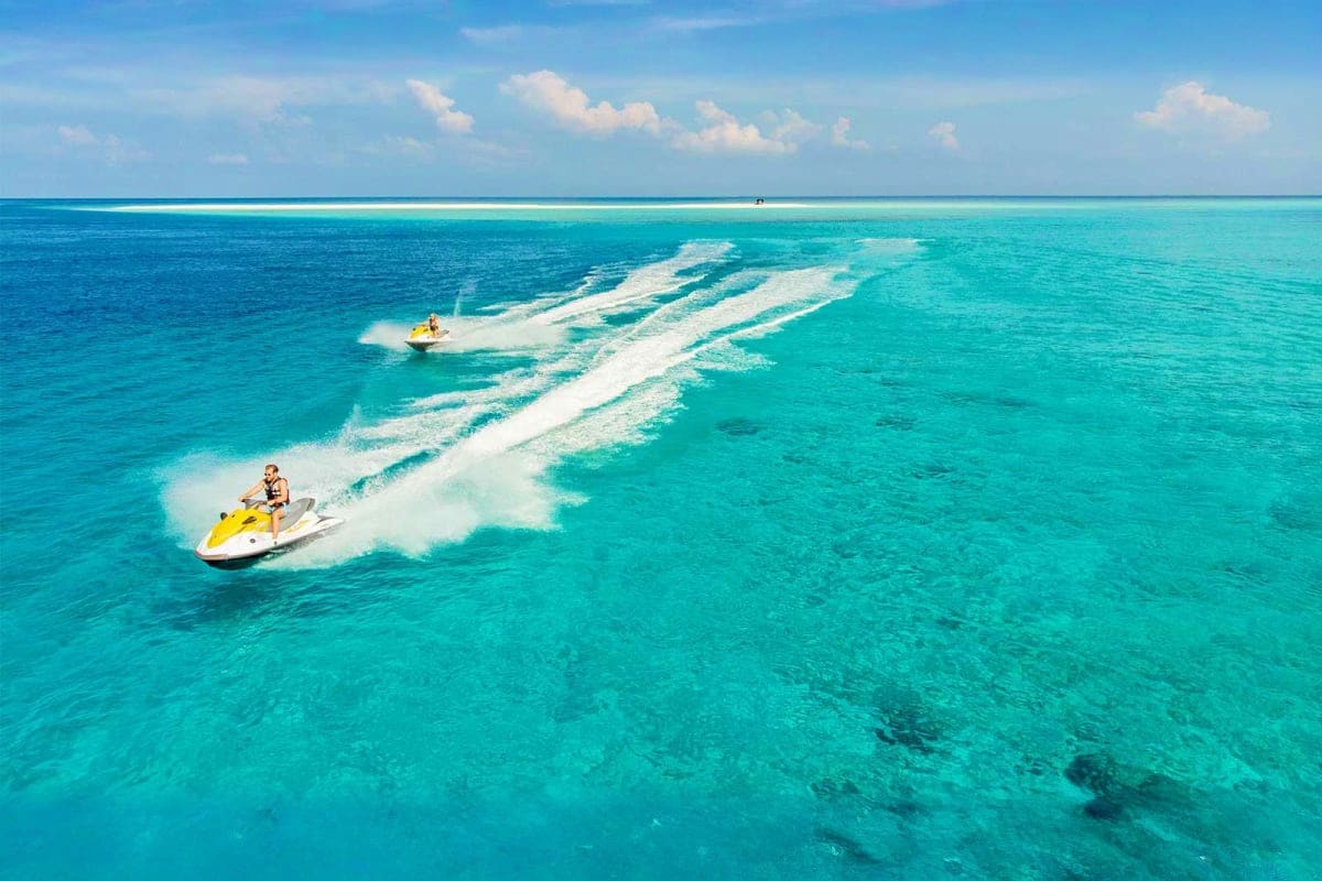 Aerial view of two yellow jet skis creating white water trails in turquoise ocean near Medhufushi Island Resort, Maldives