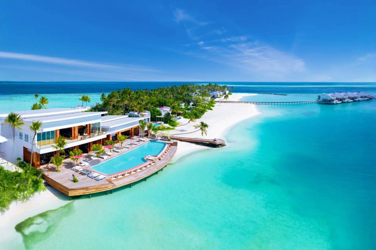 Aerial view of Medhufushi Island Resort with turquoise lagoon, beachfront pool, modern white buildings, and overwater bungalo