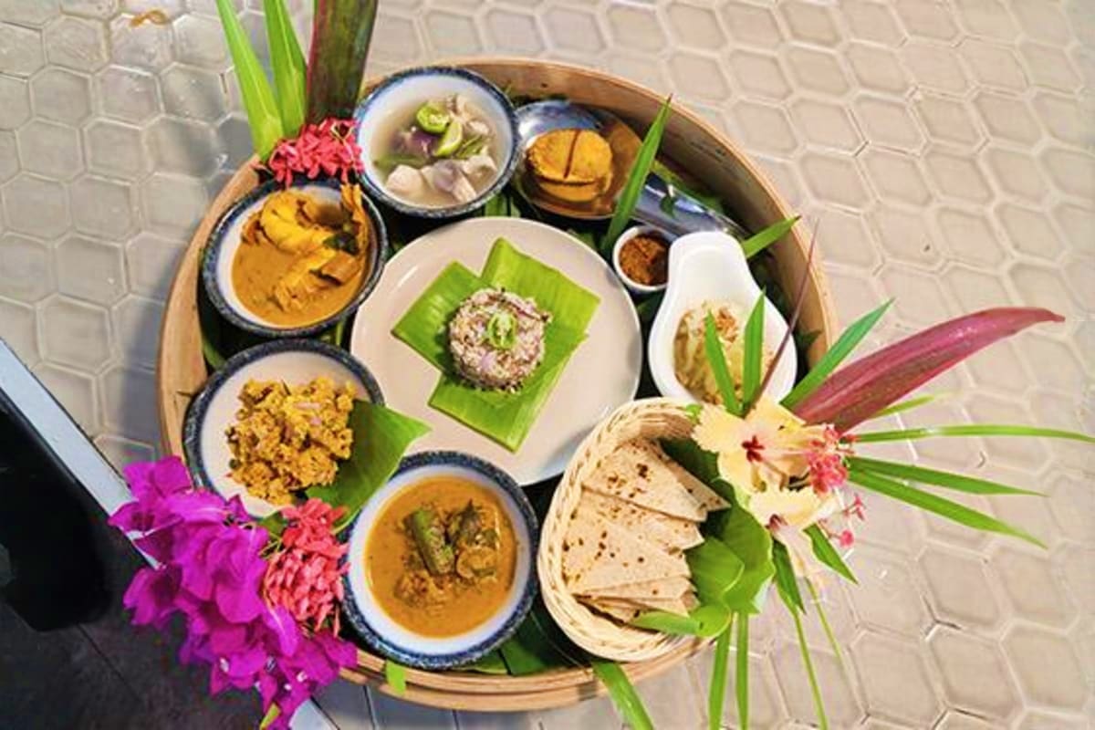 Overhead view of Thai cuisine platter with curry dishes, fresh herbs, tropical flowers, and flatbread on wooden tray
