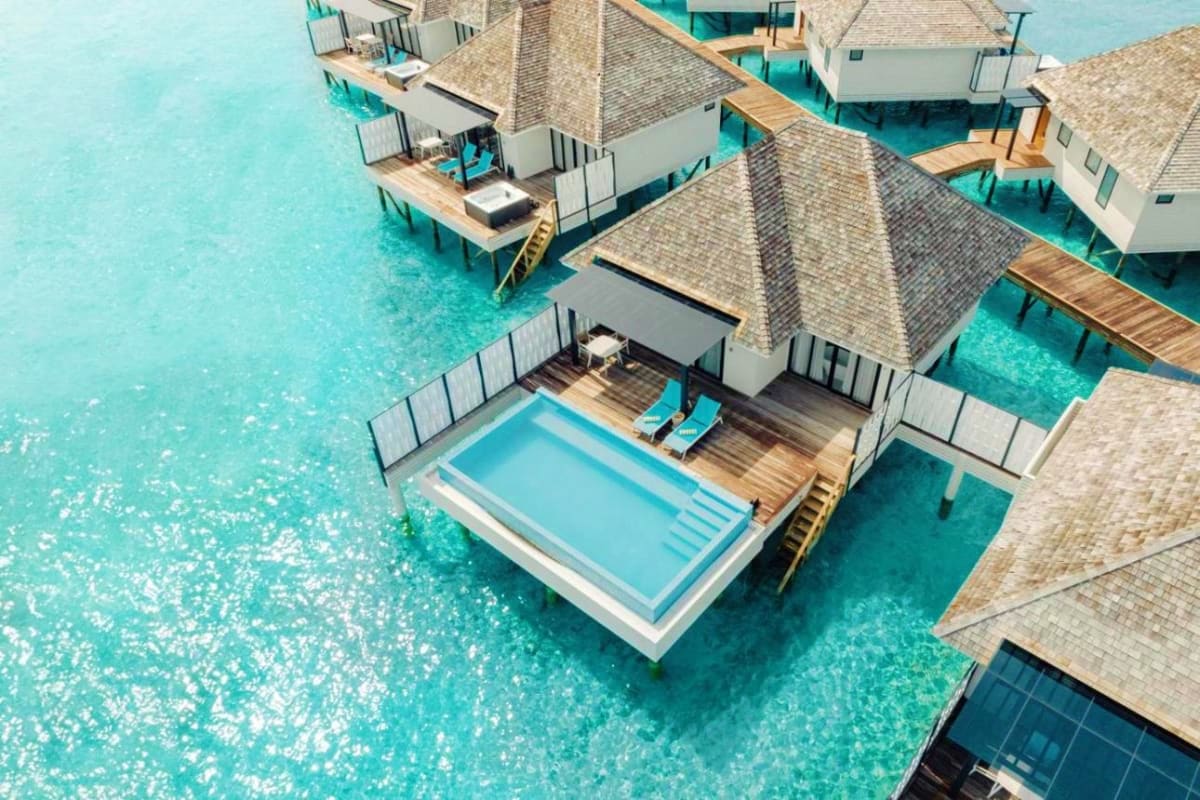 Aerial view of overwater bungalows at JW Marriott Maldives Resort with turquoise lagoon and swimming pool