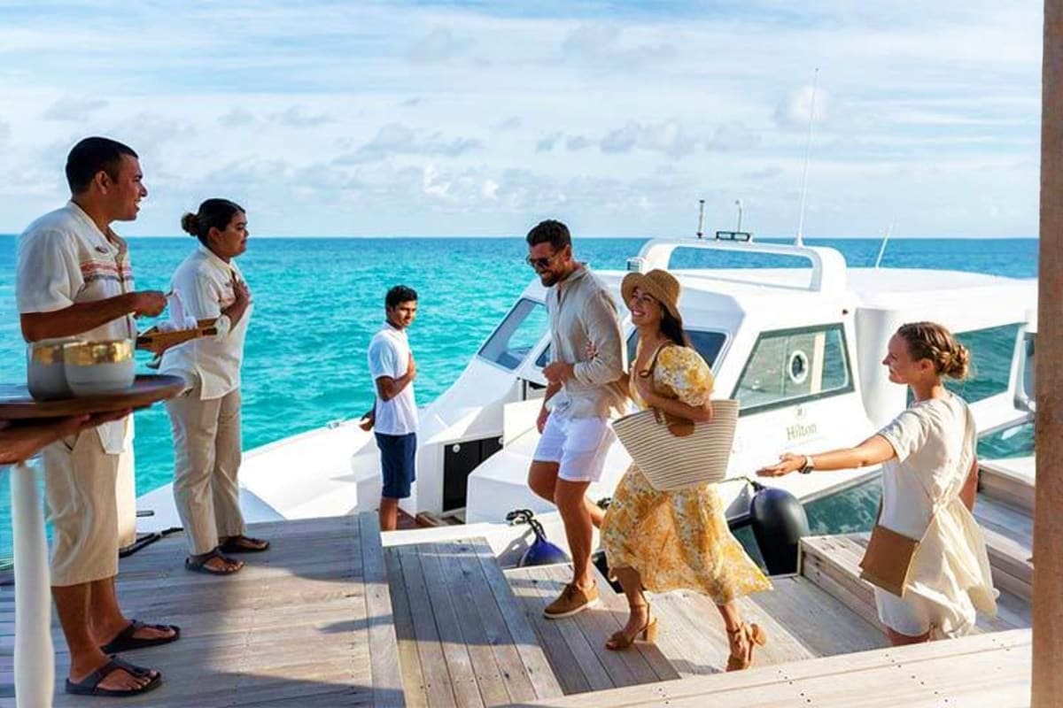 Staff greeting guests aboard a luxury speedboat at JW Marriott Maldives Resort & Spa with turquoise ocean waters in backgroun