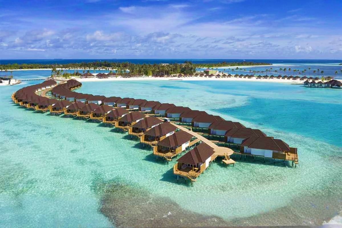 Aerial view of overwater bungalows at Sun Siyam Olhuveli Resort in turquoise lagoon waters with palm-lined island and beach i