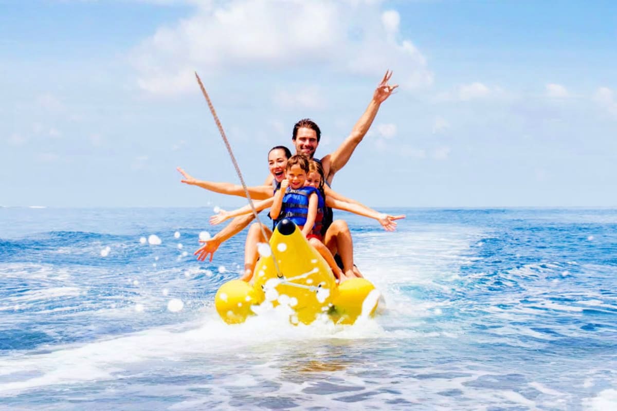 Happy family riding yellow inflatable tube in ocean waves at tropical beach resort