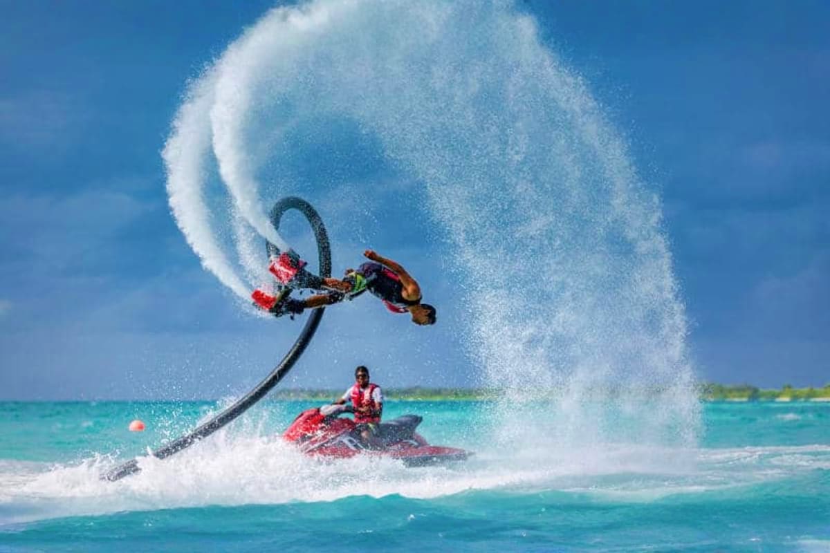 Jet ski rider performing aerial stunt with water spray at tropical beach resort in Maldives with turquoise ocean