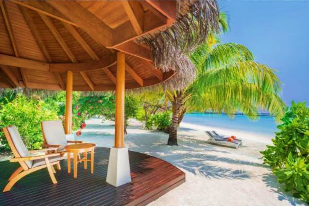 Tropical beach resort with thatched roof pavilion, wooden lounge chairs, palm trees, and turquoise ocean water at Sheraton Ma