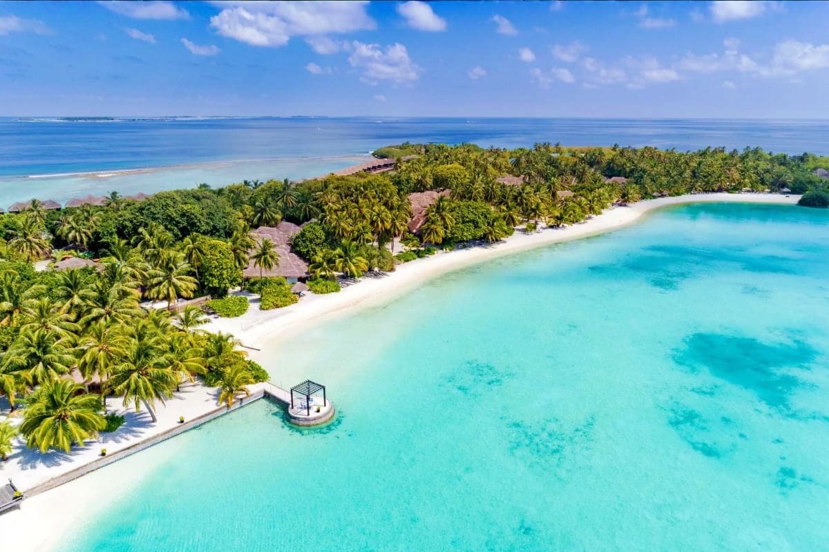 Aerial view of Sheraton Maldives Full Moon Resort with turquoise lagoon, white sand beach, palm trees, and overwater bungalow