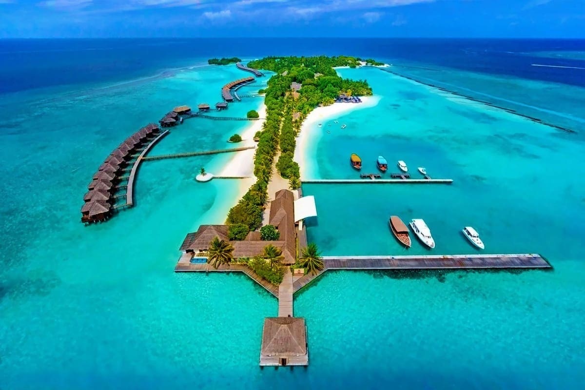 Aerial view of Sheraton Maldives Full Moon Resort with overwater bungalows, white sand beach, turquoise lagoon, and moored bo