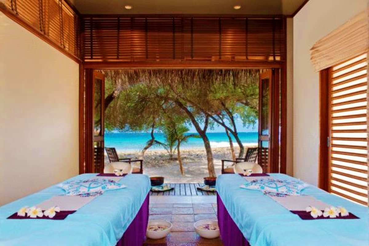 Luxury spa treatment room with two massage beds overlooking tropical beach with turquoise ocean and palm trees at Sheraton Ma