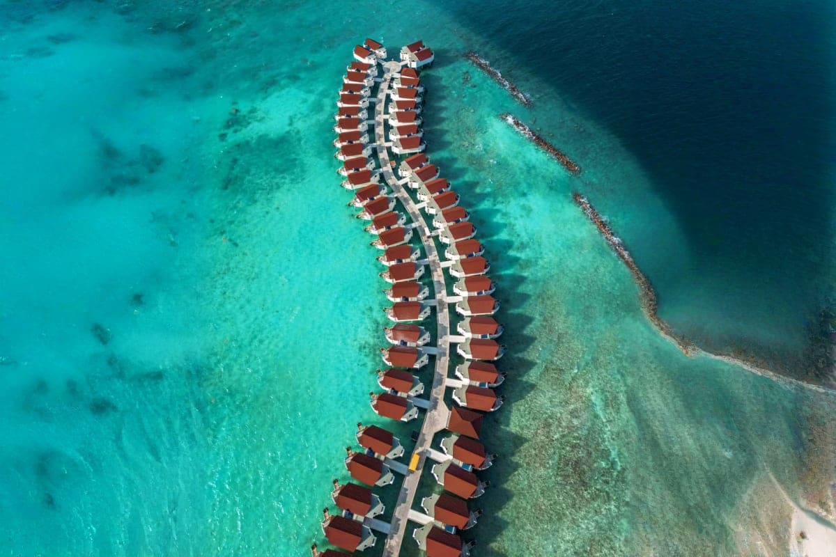 Aerial view of overwater bungalows with red roofs at Oblu Xperience Ailafushi resort in the Maldives, surrounded by turquoise