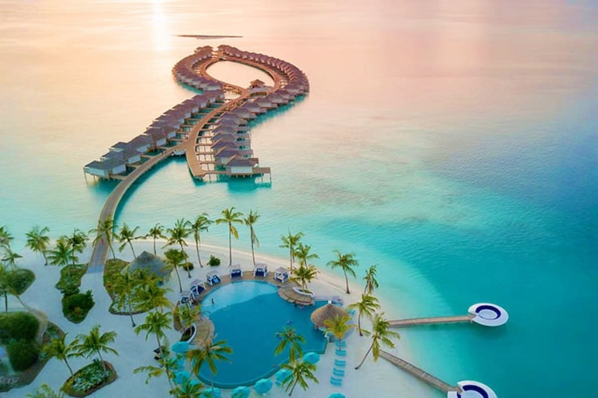 Aerial view of Oblu Xperience Ailafushi resort in the Maldives showing curved overwater bungalows, lagoon pool, and turquoise