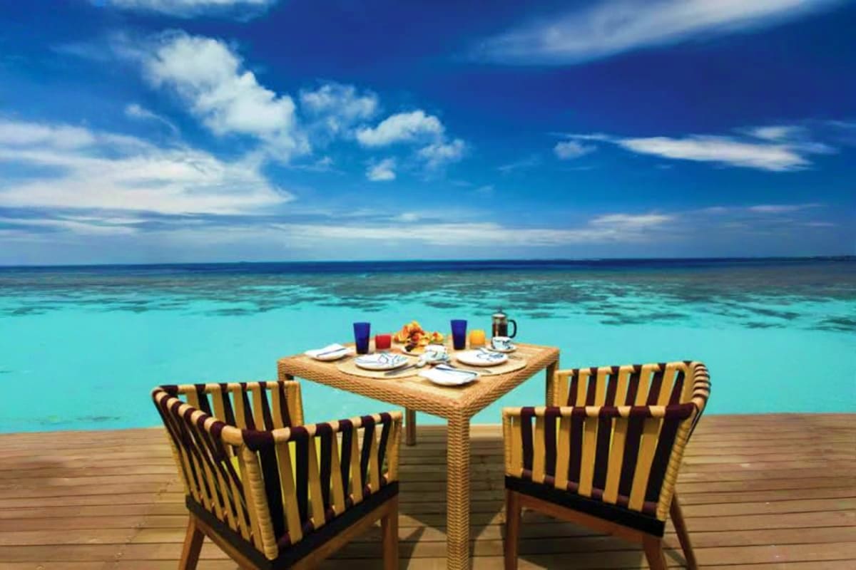 Outdoor dining table set on wooden deck with turquoise ocean and sky, Maldives resort