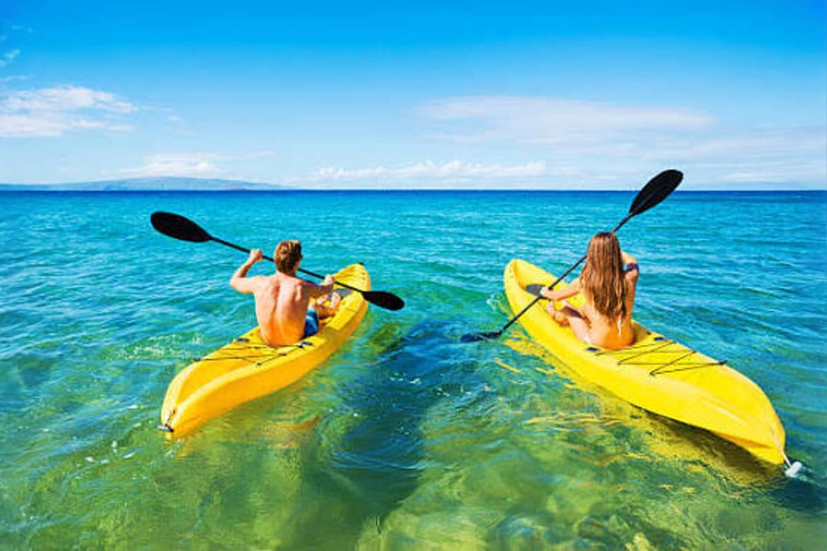 Two people kayaking on yellow kayaks in crystal clear turquoise water at a tropical beach resort in the Maldives