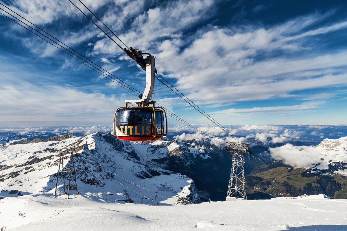 Titlis cable car suspended above snowy Alpine peaks with snow-covered mountains and valleys visible below on a clear day