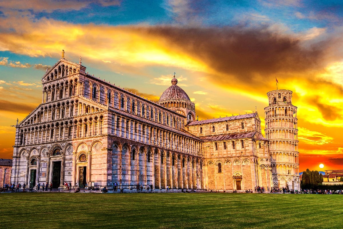 Swiss Italian Explorer Pisa Cathedral and Leaning Tower illuminated by golden sunset in Pisa, Italy with green lawn in foreground