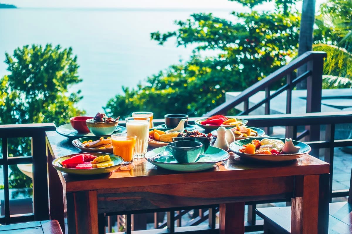 Tropical beachfront breakfast table with fresh fruit, juice, and local dishes overlooking ocean and palm trees in Seychelles