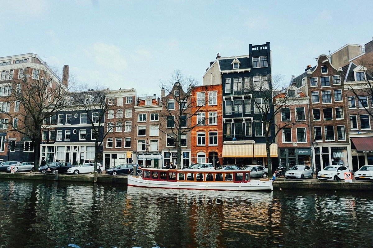 Historic Amsterdam canal with traditional Dutch architecture, colorful buildings, and a tour boat on the water