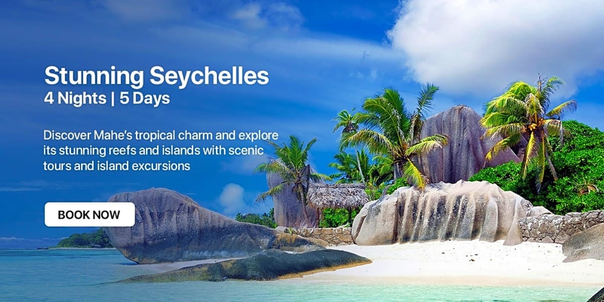 Tropical beach in Seychelles with white sand, turquoise water, distinctive granite rock formations, and palm trees under blue