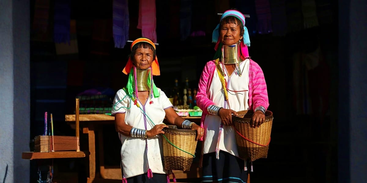 Two women from the Kayan people of northern Thailand wearing traditional brass neck rings and colorful headwear in Chiang Rai