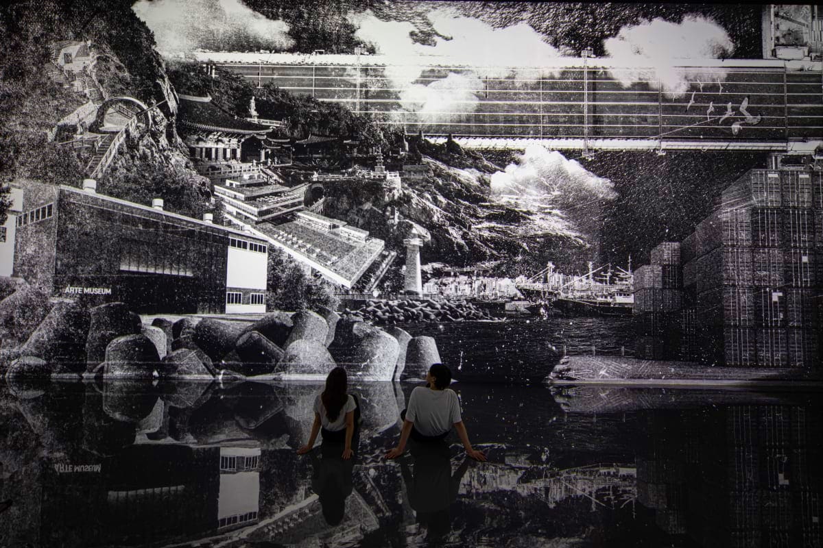 Arte Museum Dubai Two visitors viewing a large black and white mural of an Asian coastal landscape with traditional architecture and rocky shor