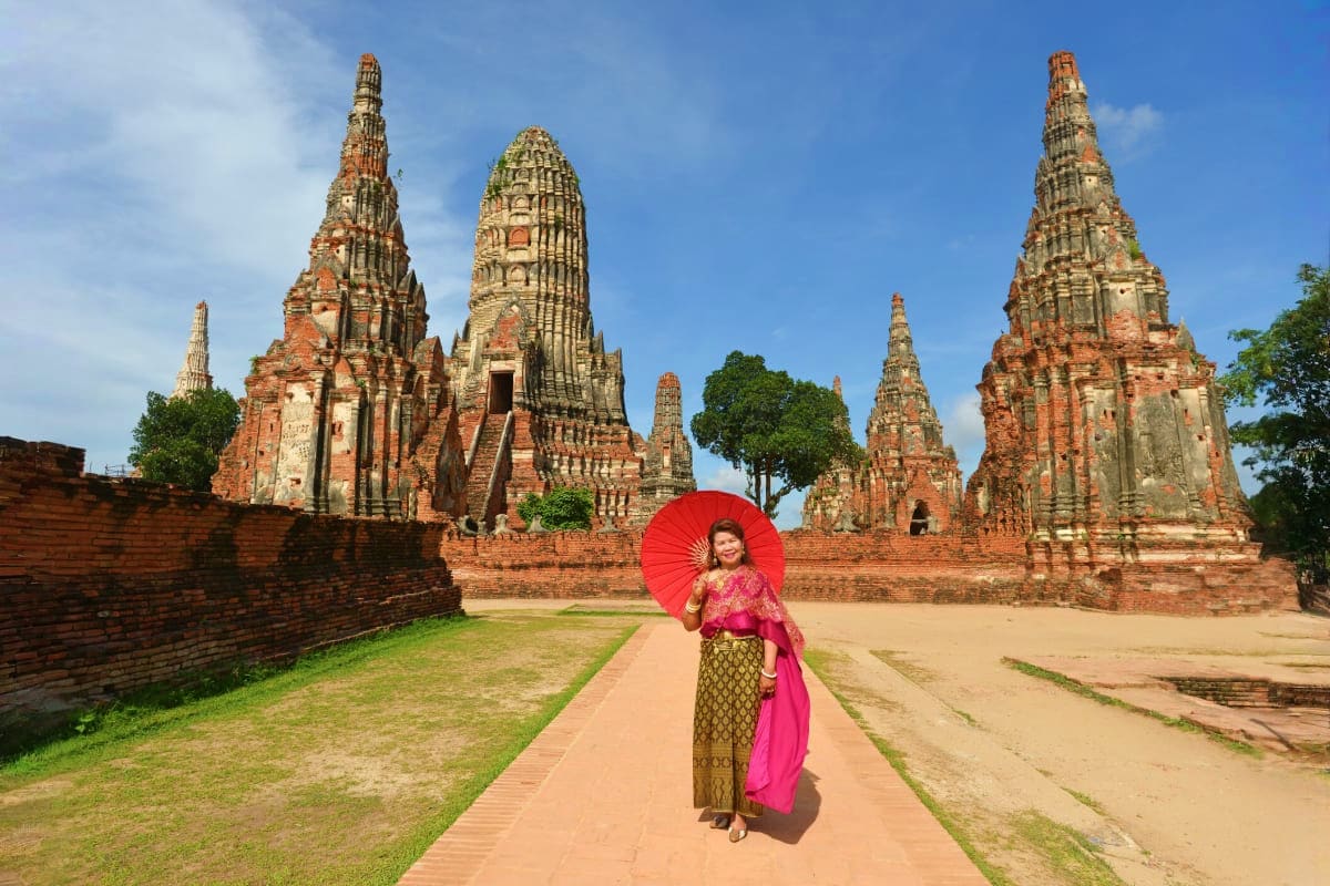 Ayutthaya Full Day Tour Woman in traditional Thai dress with red umbrella walking toward ancient temple ruins in Ayutthaya, Thailand