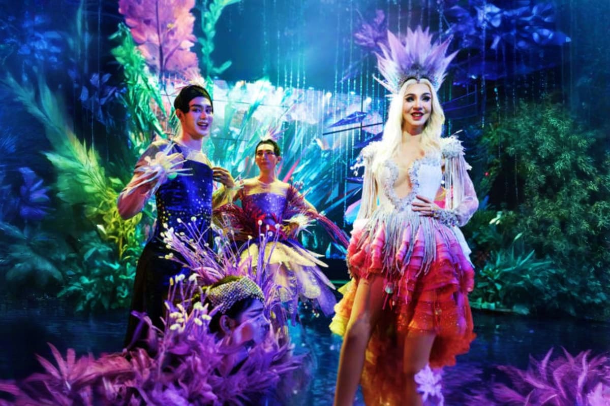 Tiffany Show Pattaya Performers in elaborate sequined costumes and headdresses on an illuminated stage with colorful neon lighting and tropical fo