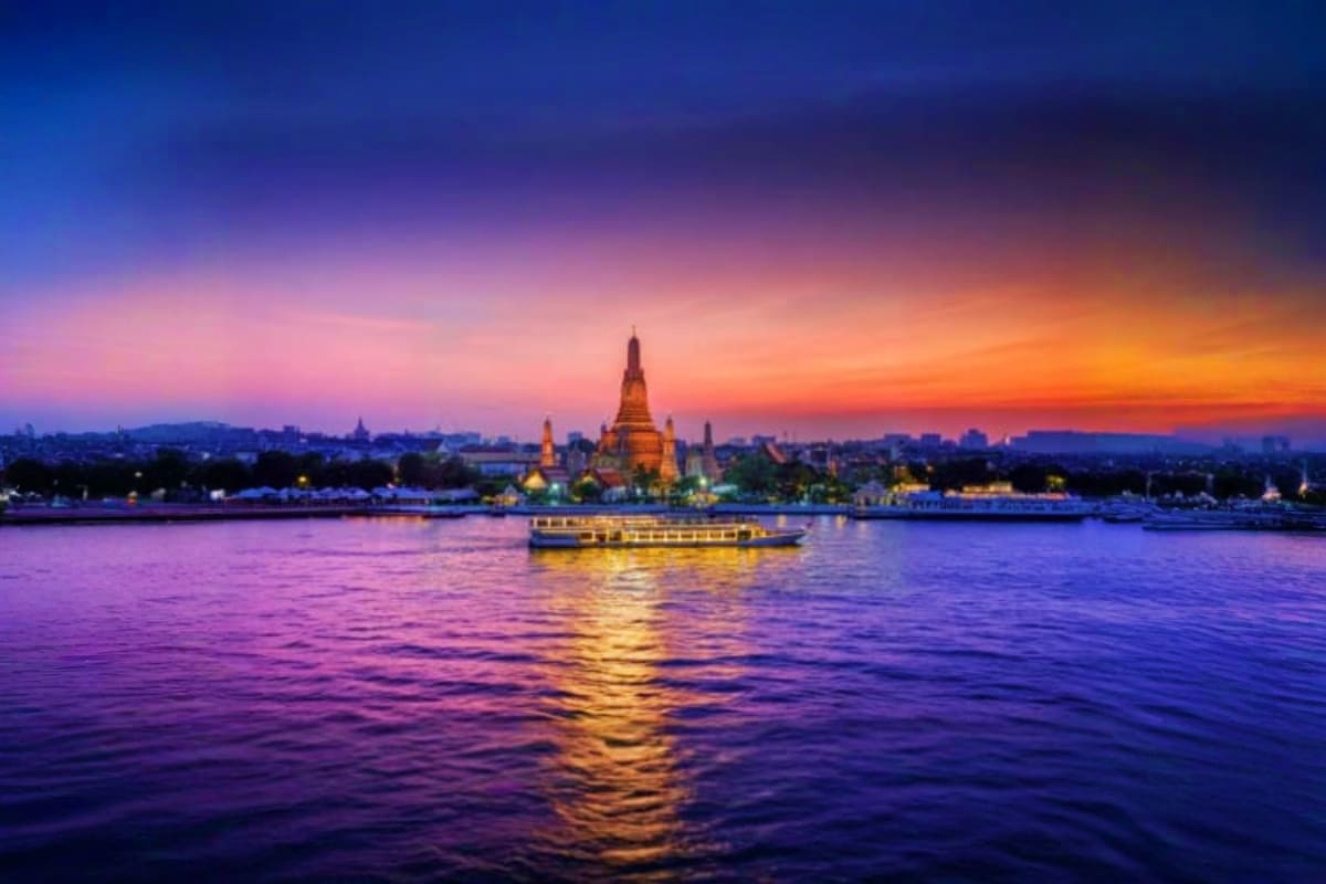 Wat Arun temple illuminated at sunset across the Chao Phraya River with a tour boat in Bangkok, Thailand