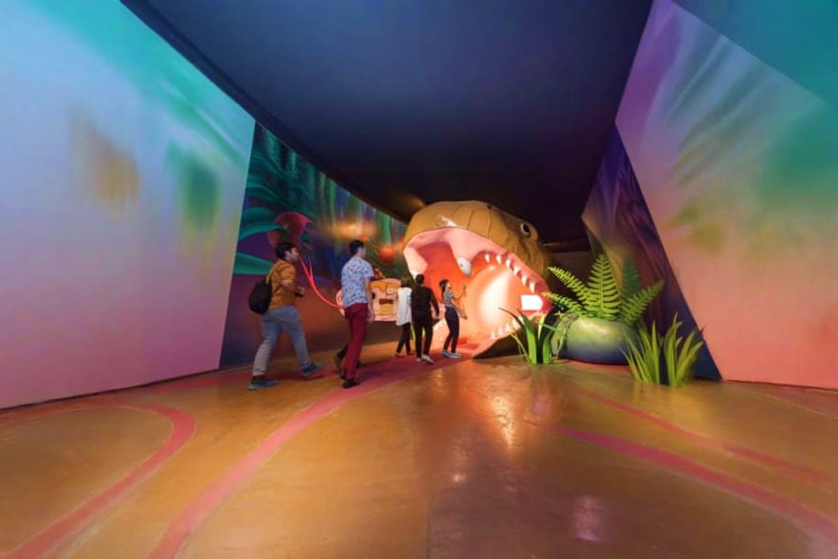 Siam Serpentarium Visitors exploring an interactive indoor exhibit featuring a large illuminated red snake sculpture with tropical plants and c