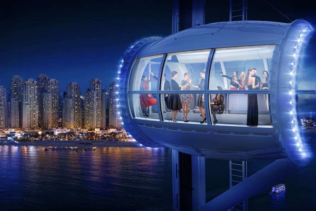 Group of people inside illuminated observation pod of Ain Dubai wheel overlooking nighttime city skyline and waterfront