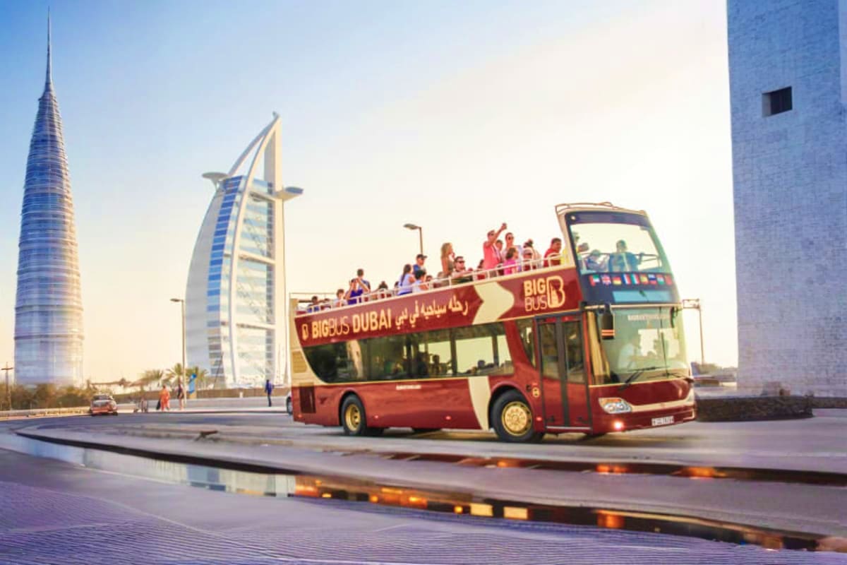 Red double-decker Big Bus tour bus passing Burj Al Arab luxury hotel in Dubai with tourists on upper deck