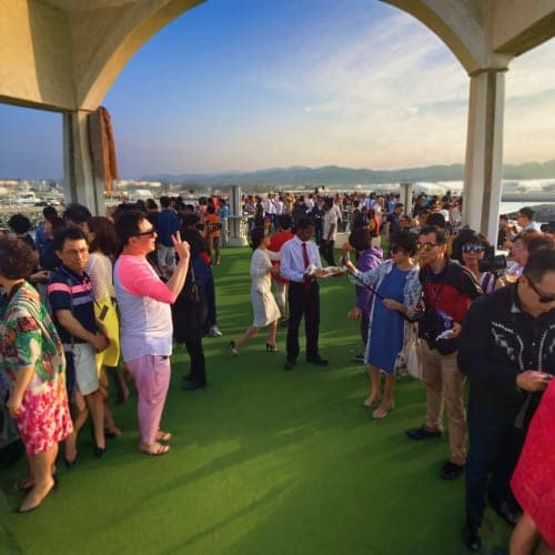 New Years Eve On Lotus Megayacht Large group of people gathered on green deck of luxury yacht with city skyline and mountains visible in background at dusk