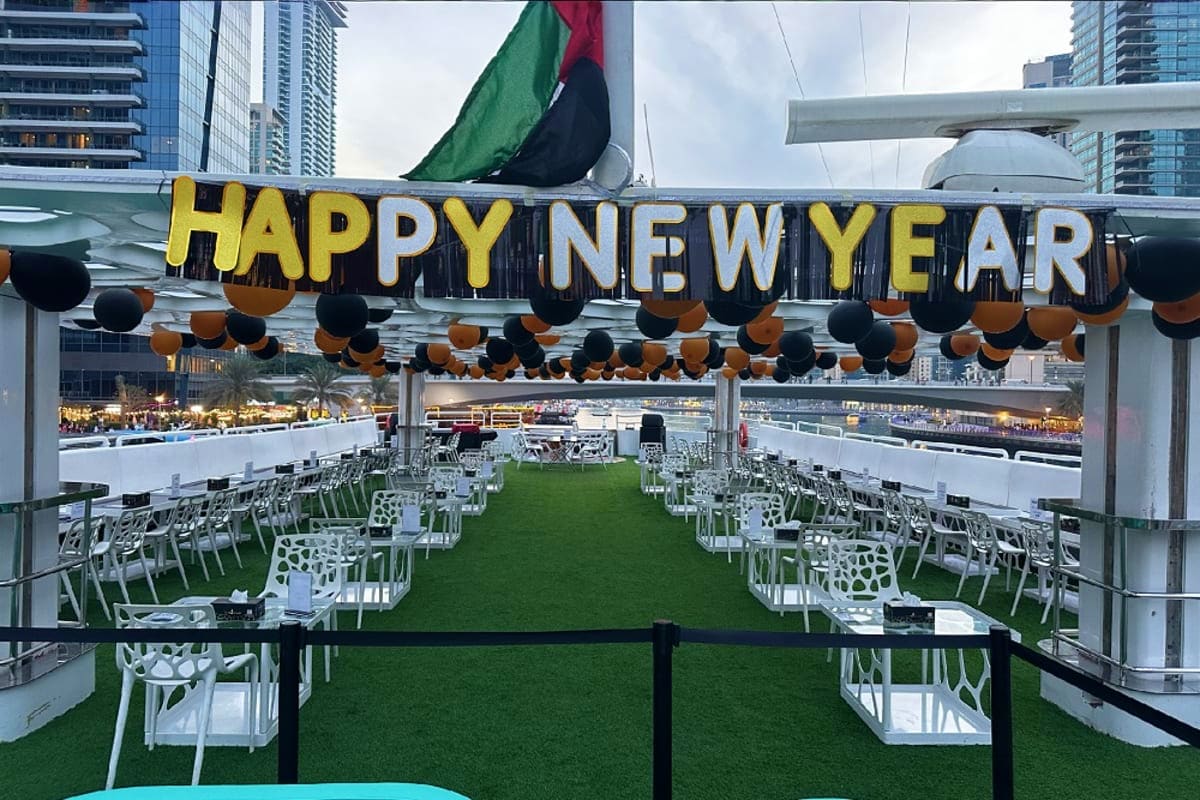 New Years Eve On Lotus Megayacht Rooftop deck of Lotus Megayacht decorated with gold "Happy New Year" banner and black and gold balloons, with white chairs ar
