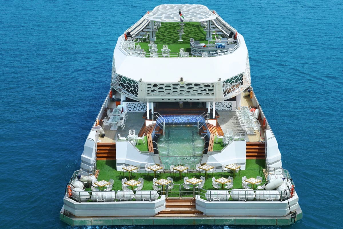 New Years Eve On Lotus Megayacht Aerial view of luxury megayacht with multiple deck levels featuring pools, dining areas, and manicured green spaces surrounde