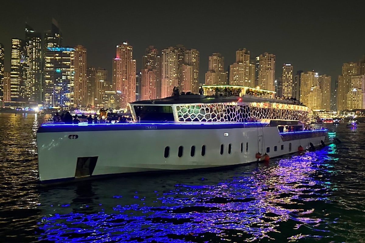 Illuminated white luxury megayacht with blue LED lights on water at night, Chicago skyline in background