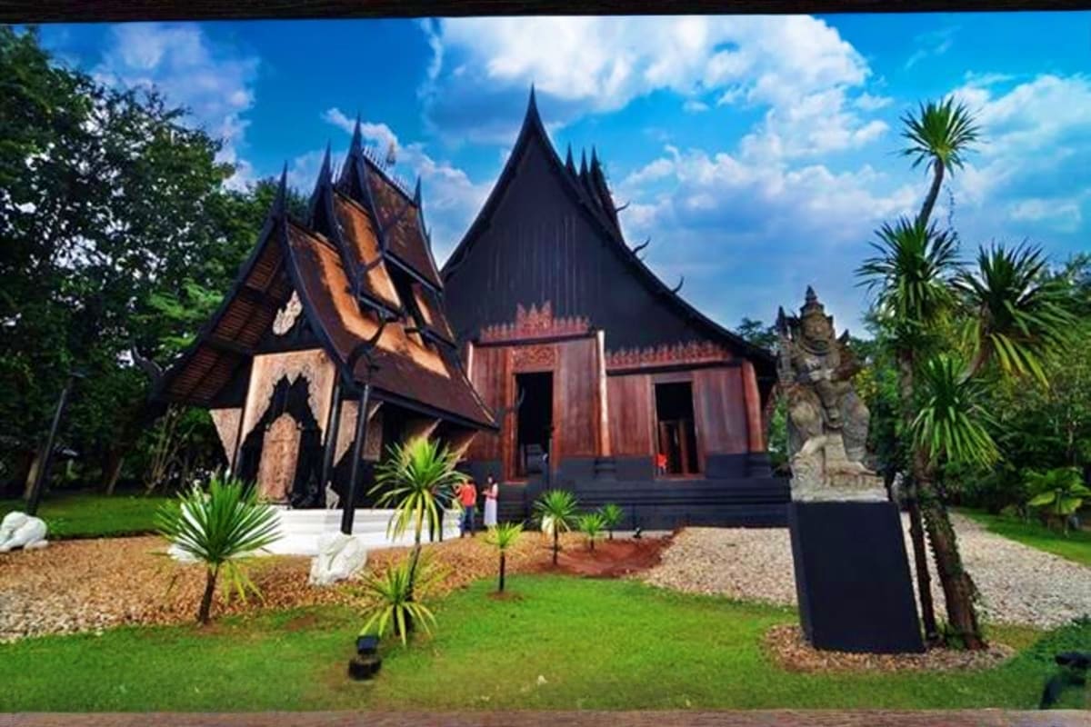 Traditional Thai temple with distinctive black peaked roofs, ornate wooden architecture, and tropical palm trees in surroundi