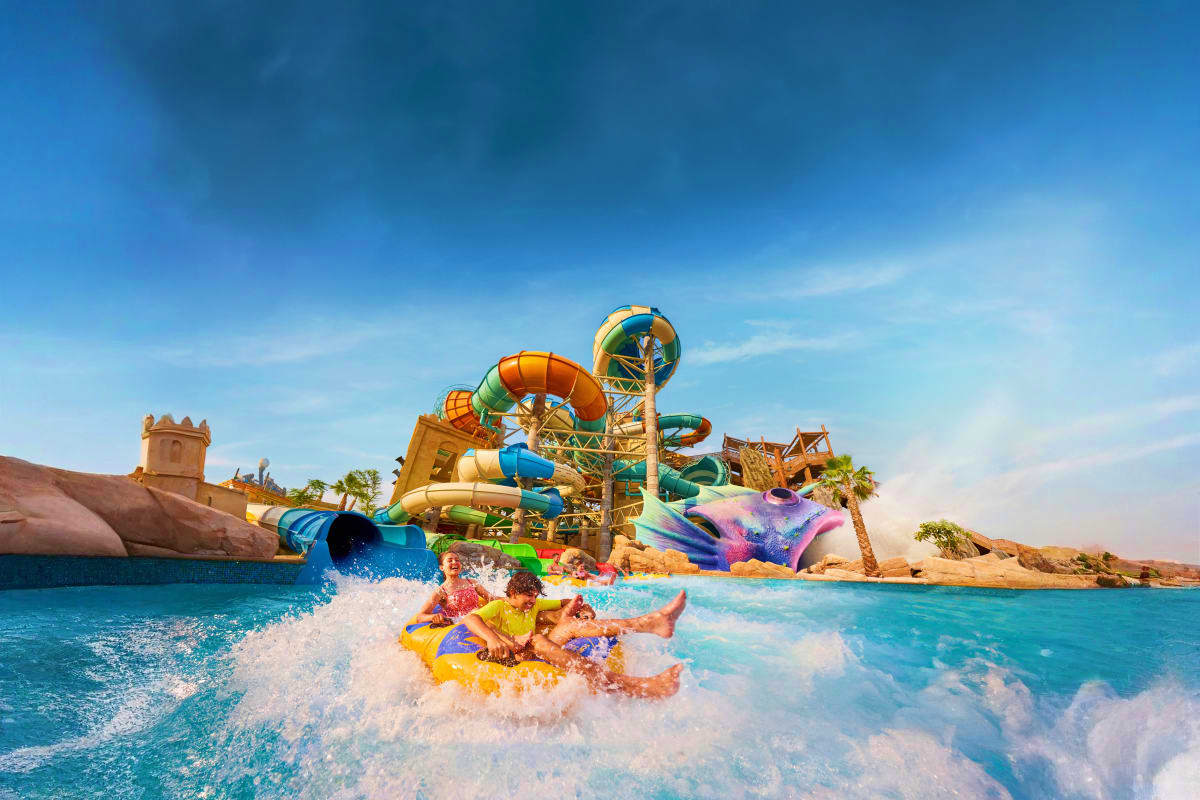 Yas Waterworld Children splashing in turquoise water at Yas Waterworld with colorful water slides and themed attractions in background under