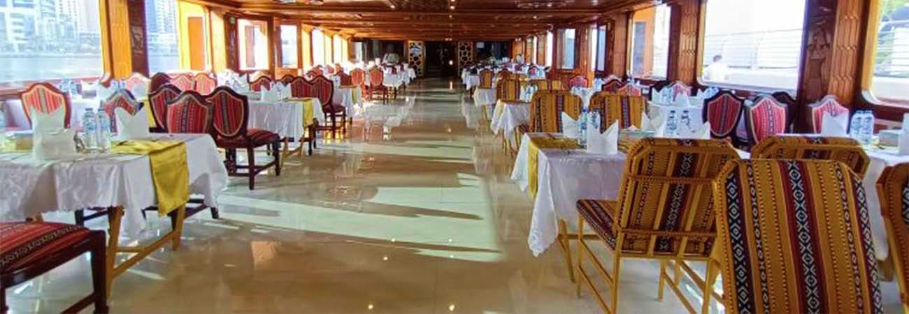 Elegant ship dining room with white tablecloths, ornate chairs, and panoramic windows overlooking the cityscape