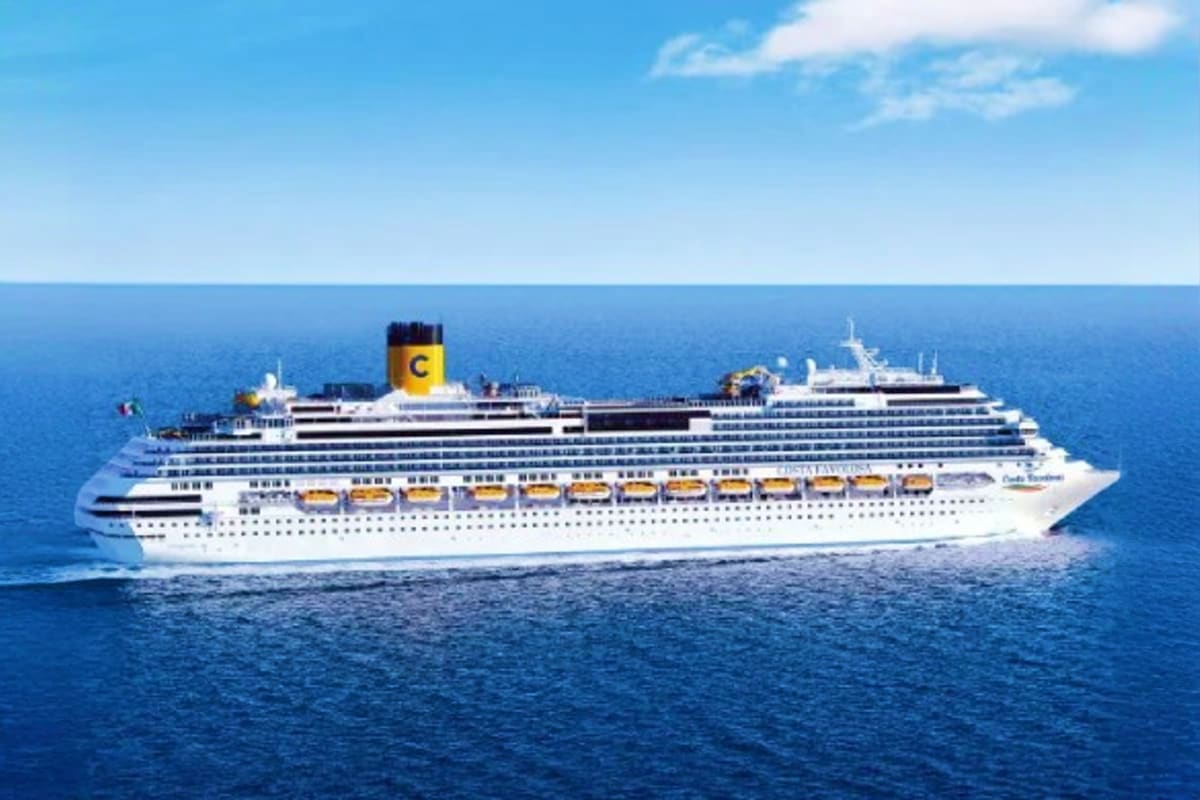 Large white cruise ship with yellow funnel on open ocean under blue sky