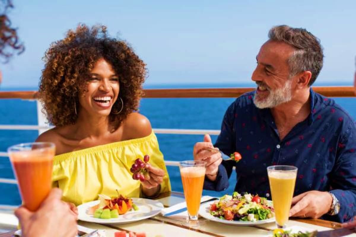 Couple enjoying lunch on a cruise ship deck overlooking the ocean with fresh salads and tropical drinks