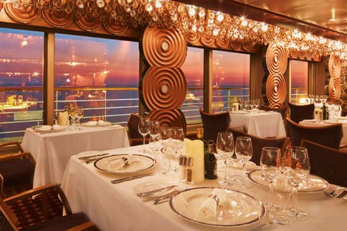 Elegant fine dining restaurant on Costa Favolosa with sunset cityscape view through floor-to-ceiling windows, formal place se